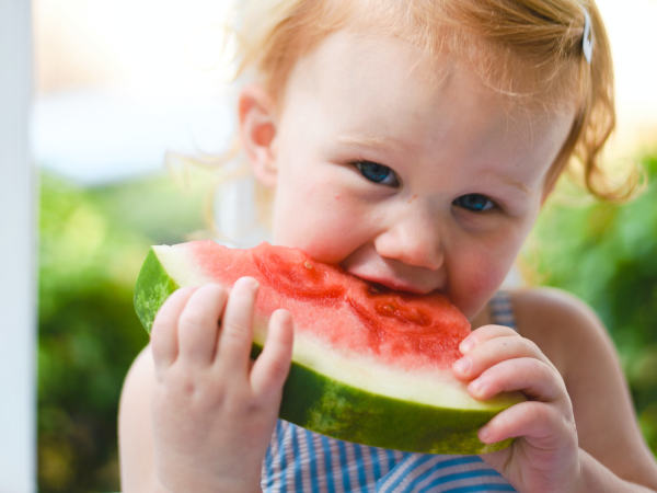 Ein Baby isst ein Stück Wassermelone.