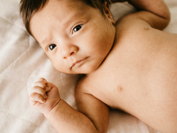 Ein Baby in Rückenlage mit braunen Haaren und dunklen Augen.